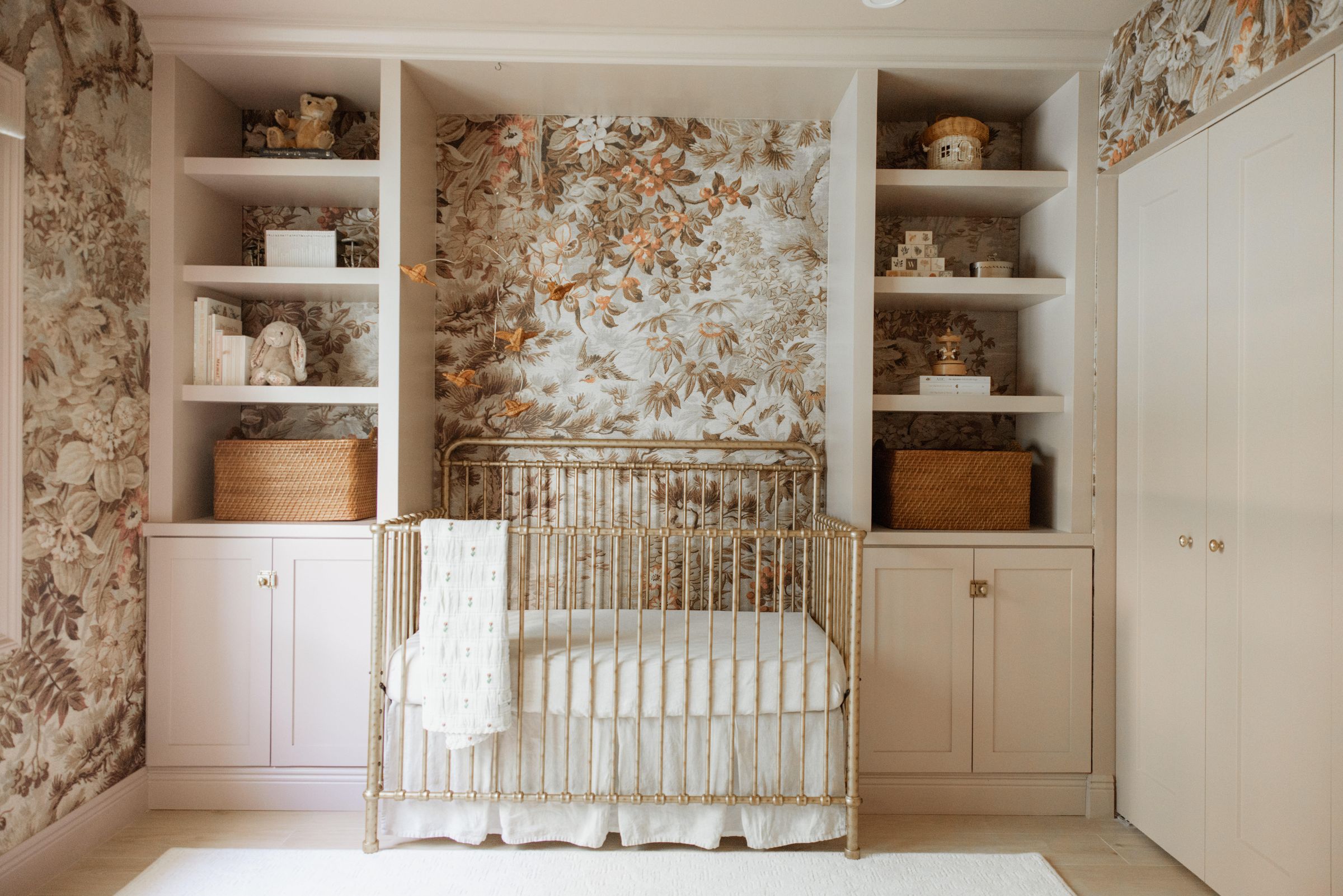Vintage botanical nursery designed by Casa Collective — antique brass crib, floral wallpaper, built-in shelving