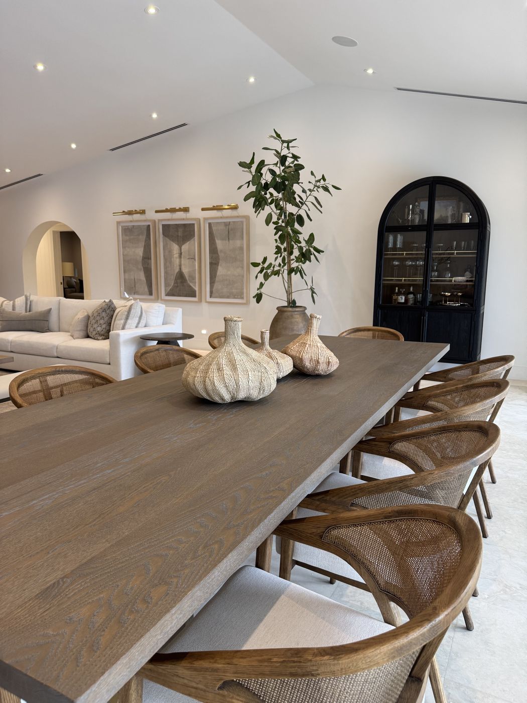 Dining table with cane-back chairs and woven vases, arched black cabinet behind