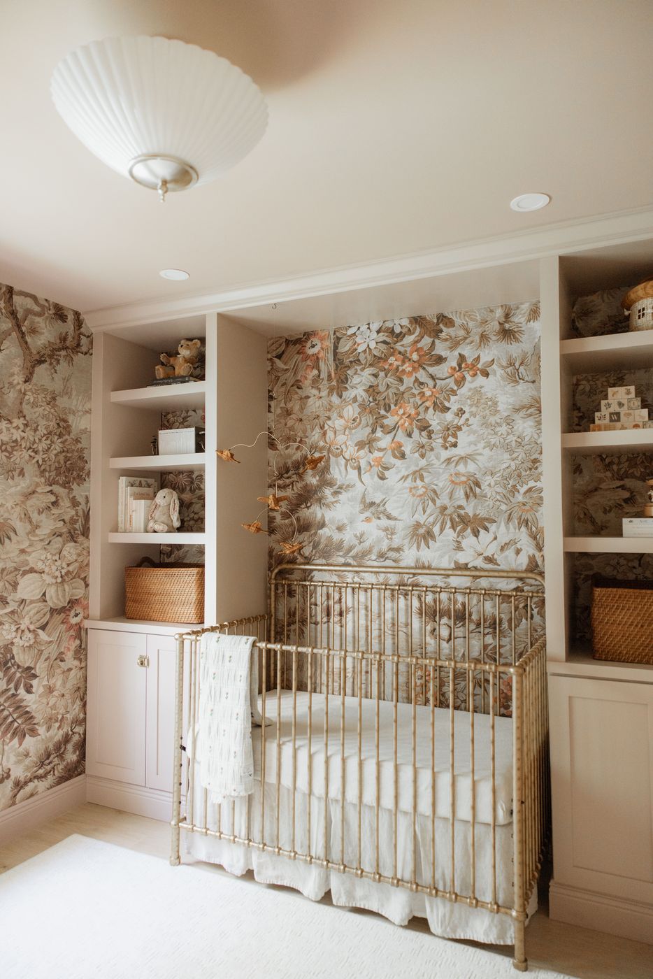 Nursery with botanical wallpaper, brass crib, and bird mobile